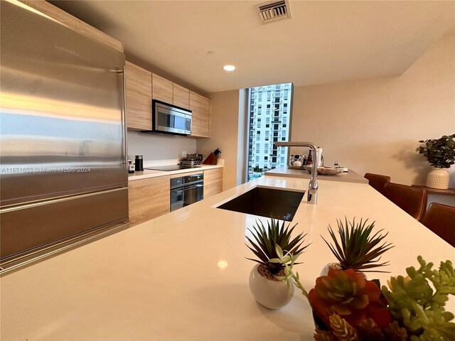 kitchen featuring a kitchen breakfast bar, light brown cabinetry, appliances with stainless steel finishes, kitchen peninsula, and sink