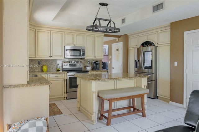 kitchen with a center island, light stone counters, stainless steel appliances, and cream cabinets