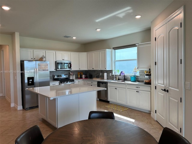 kitchen with light tile patterned floors, a center island, stainless steel appliances, sink, and decorative backsplash