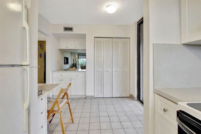 kitchen featuring white refrigerator, light tile patterned floors, a textured ceiling, and white cabinets