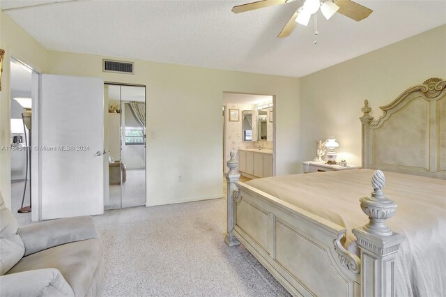 carpeted bedroom with a textured ceiling, ensuite bathroom, ceiling fan, and a closet