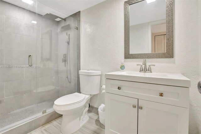 bathroom with a shower with door, vanity, and toilet