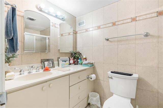 bathroom with vanity, toilet, tile walls, and a shower with door