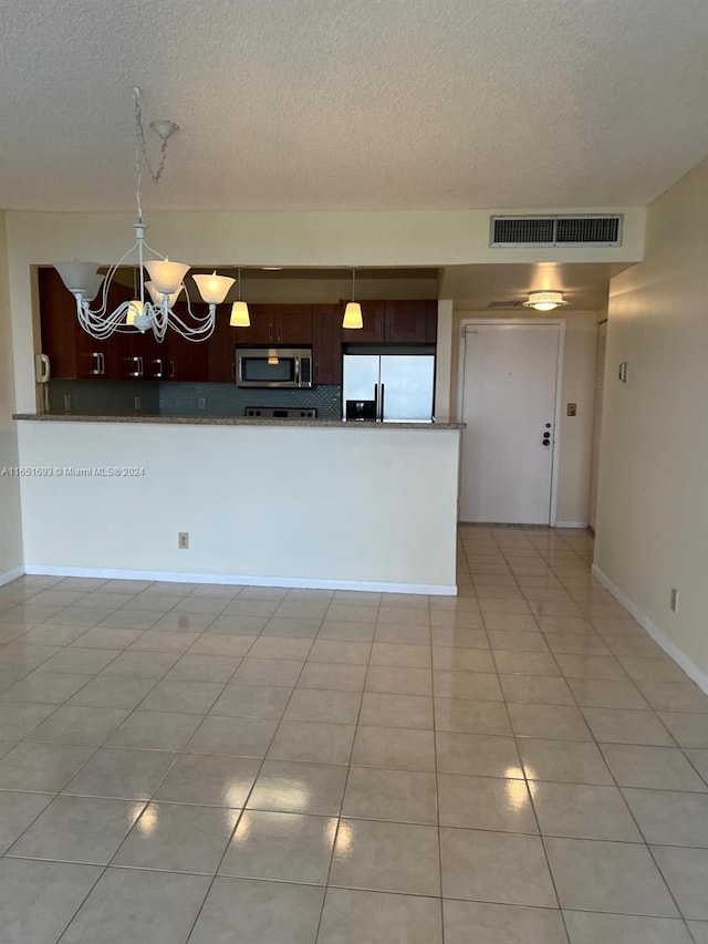 kitchen with appliances with stainless steel finishes, a textured ceiling, light tile patterned floors, and an inviting chandelier