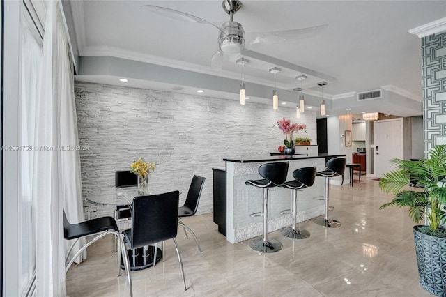 interior space with ornamental molding, a kitchen breakfast bar, ceiling fan, and hanging light fixtures