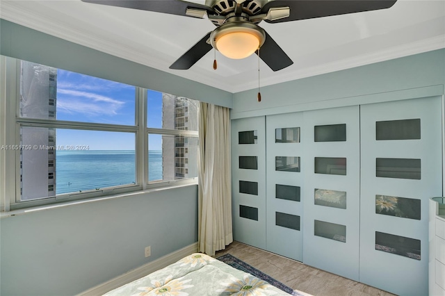 unfurnished bedroom with light wood-type flooring, a water view, a closet, ceiling fan, and ornamental molding