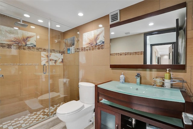 bathroom featuring vanity, toilet, walk in shower, and tile walls