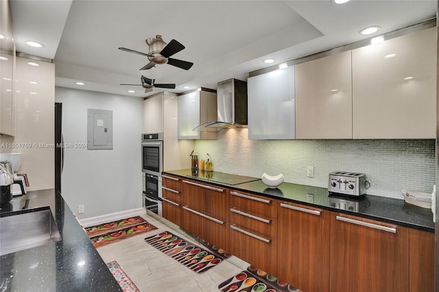 kitchen with black electric stovetop, backsplash, electric panel, ceiling fan, and wall chimney range hood