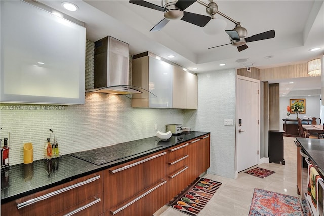 kitchen featuring dark stone countertops, backsplash, ceiling fan, wall chimney exhaust hood, and black electric stovetop