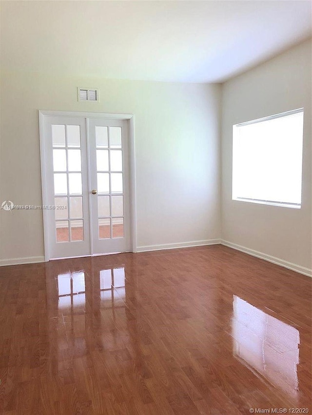 empty room featuring a wealth of natural light, dark hardwood / wood-style floors, and french doors
