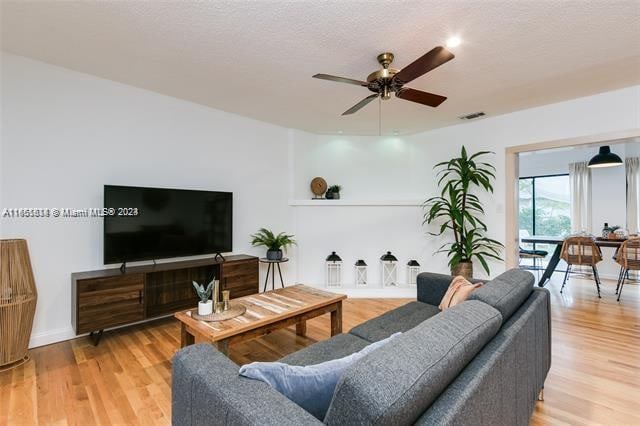 living room featuring light wood-type flooring, a textured ceiling, and ceiling fan