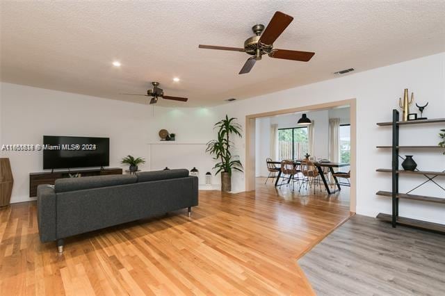 living room with a textured ceiling, ceiling fan, and light hardwood / wood-style floors