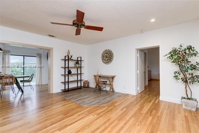 living area with ceiling fan, light hardwood / wood-style floors, and a textured ceiling