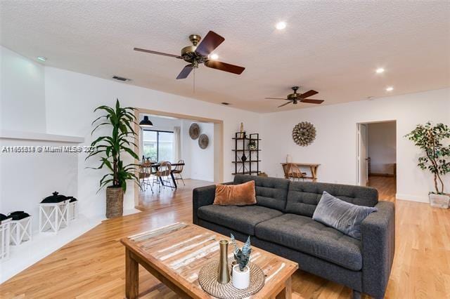 living room featuring a textured ceiling, ceiling fan, and light hardwood / wood-style floors