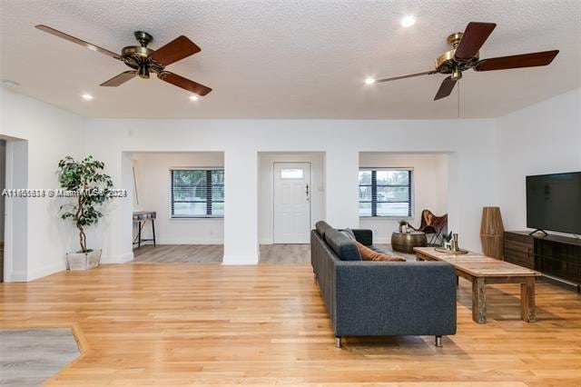 living room with light wood-type flooring, ceiling fan, and a textured ceiling