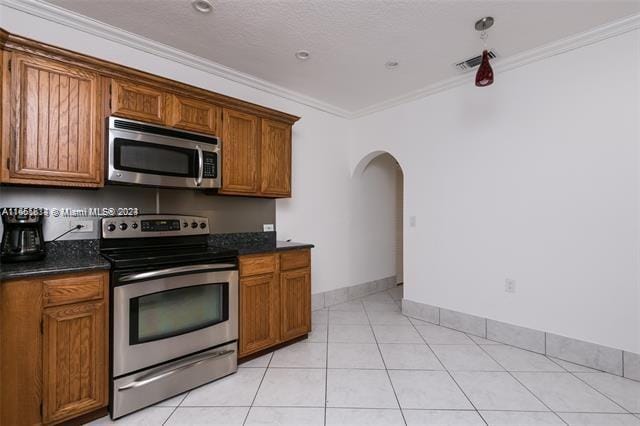 kitchen featuring ornamental molding, appliances with stainless steel finishes, light tile patterned floors, and dark stone counters