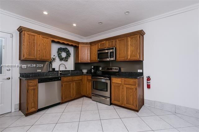 kitchen with ornamental molding, dark stone counters, stainless steel appliances, and sink