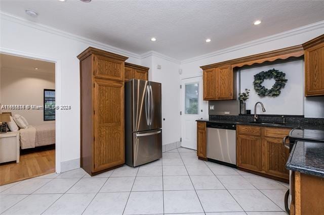 kitchen with dark stone countertops, crown molding, stainless steel appliances, light tile patterned flooring, and a textured ceiling