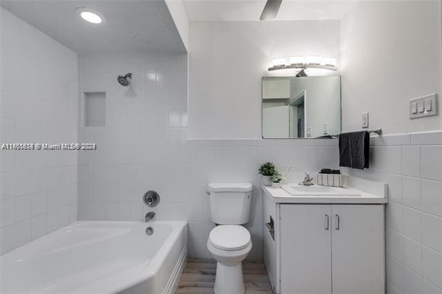 full bathroom with vanity, tile walls, toilet, hardwood / wood-style flooring, and tiled shower / bath combo