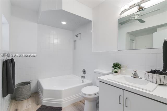 full bathroom with vanity, hardwood / wood-style floors, tile walls, toilet, and ceiling fan