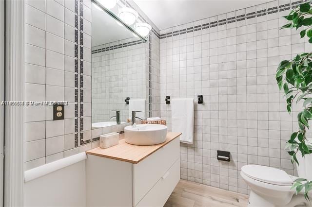 bathroom with tile walls, toilet, hardwood / wood-style flooring, and vanity