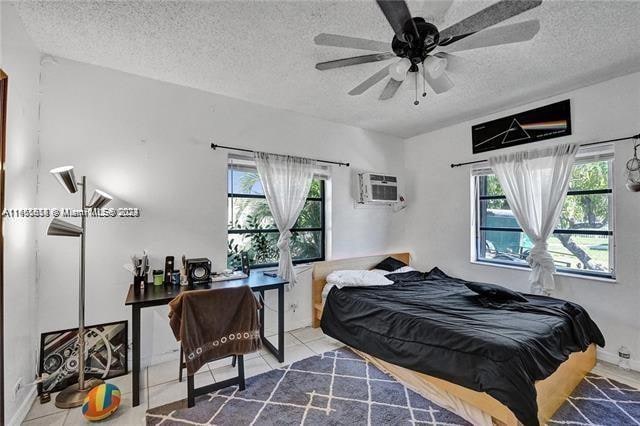 bedroom with a textured ceiling, an AC wall unit, ceiling fan, and tile patterned floors