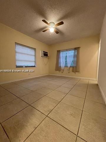 empty room with a wall mounted AC, a textured ceiling, light tile patterned floors, and ceiling fan