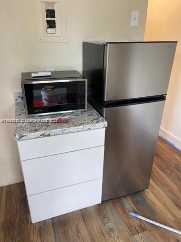 kitchen with dark wood-type flooring, light stone countertops, stainless steel refrigerator, and white cabinets