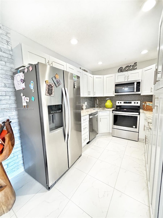 kitchen featuring light stone counters, stainless steel appliances, white cabinets, and decorative backsplash