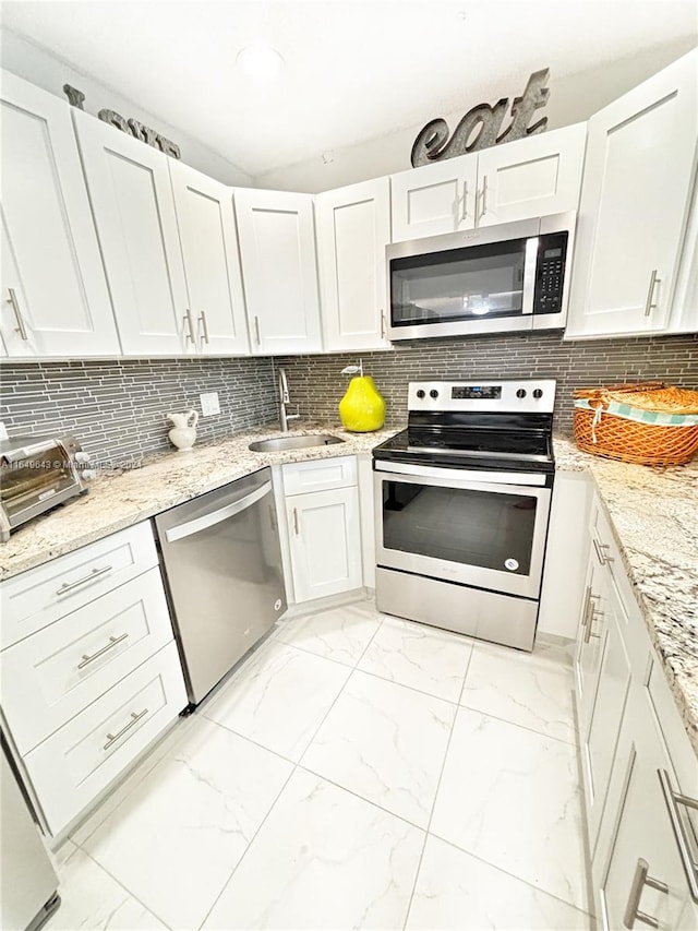 kitchen with white cabinets, backsplash, light stone countertops, stainless steel appliances, and sink