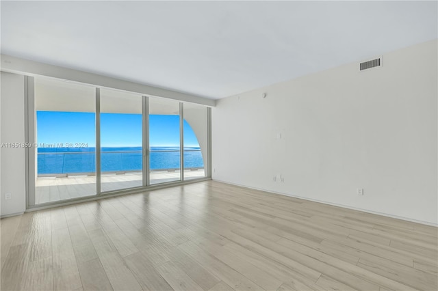 spare room with a wall of windows, light wood-type flooring, a water view, and a wealth of natural light