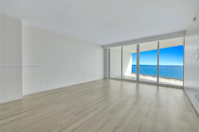 spare room featuring a wall of windows, light hardwood / wood-style flooring, and a water view