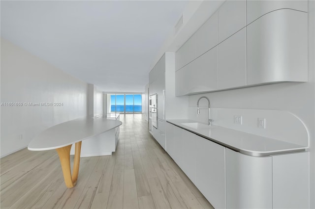 kitchen with expansive windows, white cabinets, sink, and light hardwood / wood-style floors