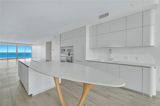 kitchen with a wall of windows, light hardwood / wood-style floors, white cabinets, a breakfast bar, and sink