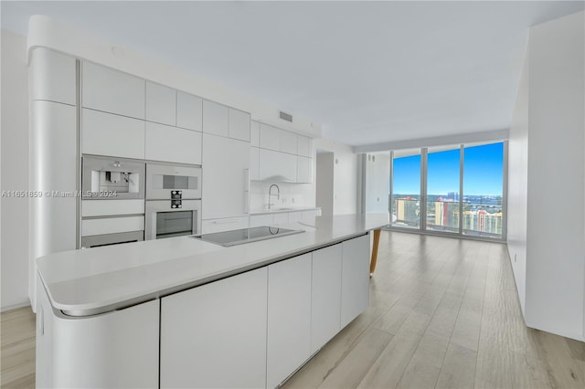 kitchen featuring light wood-type flooring, a center island, white cabinets, black electric cooktop, and expansive windows