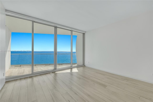 unfurnished room featuring expansive windows, light wood-type flooring, and a water view