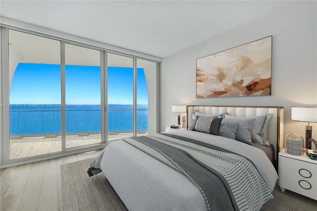 bedroom with floor to ceiling windows, hardwood / wood-style floors, and a water view