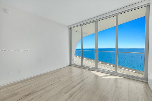 empty room with light wood-type flooring, a water view, a healthy amount of sunlight, and floor to ceiling windows