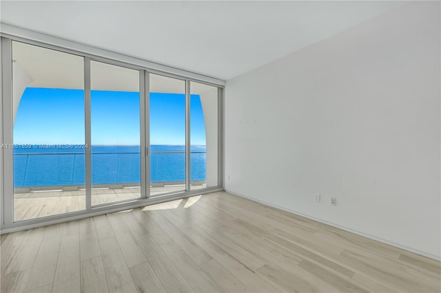 empty room featuring a wall of windows, light hardwood / wood-style floors, and a water view