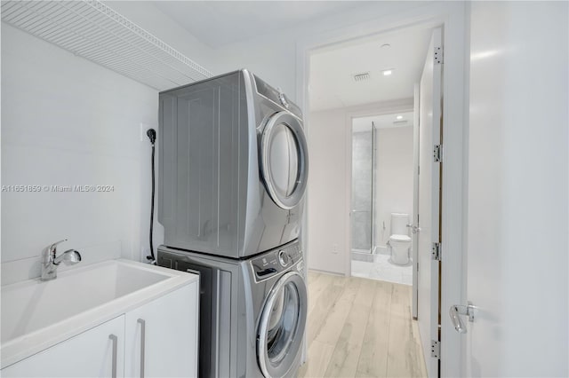 clothes washing area featuring light wood-type flooring, stacked washer / dryer, and sink