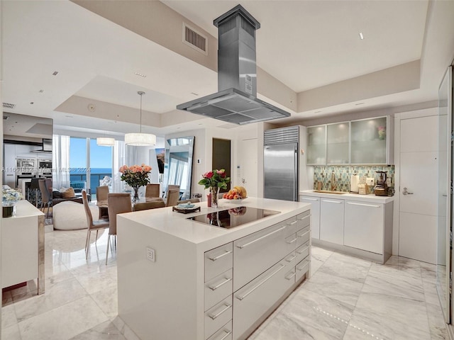 kitchen featuring a tray ceiling, built in refrigerator, black electric stovetop, a kitchen island, and island range hood