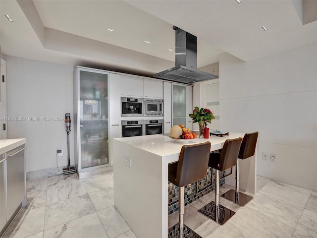 kitchen featuring island exhaust hood, a kitchen bar, a center island, stainless steel appliances, and white cabinetry