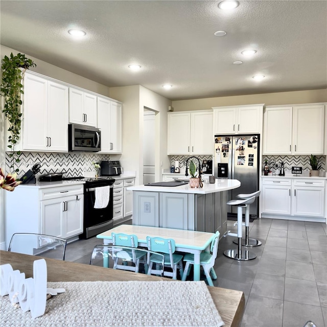 8123 NW 78th St, Tamarac, FL 33321 - kitchen featuring appliances with stainless steel finishes, tasteful backsplash, white cabinets, a textured ceiling, and an island with sink