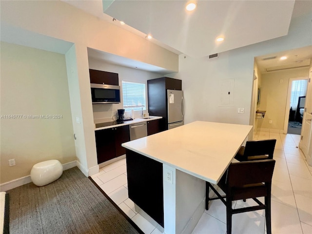 kitchen with a breakfast bar, a center island, appliances with stainless steel finishes, light tile patterned flooring, and light countertops