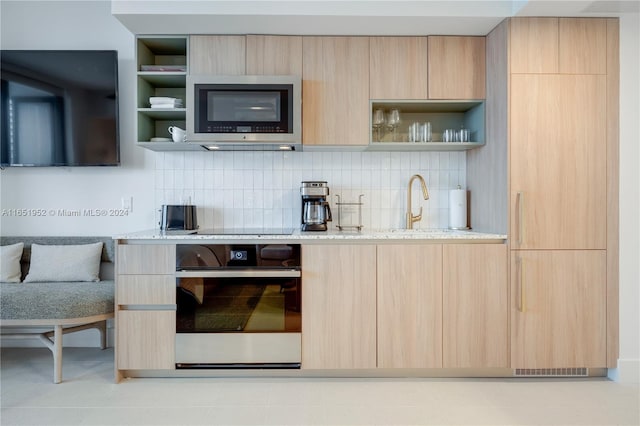 kitchen with appliances with stainless steel finishes, light brown cabinets, light stone countertops, and decorative backsplash