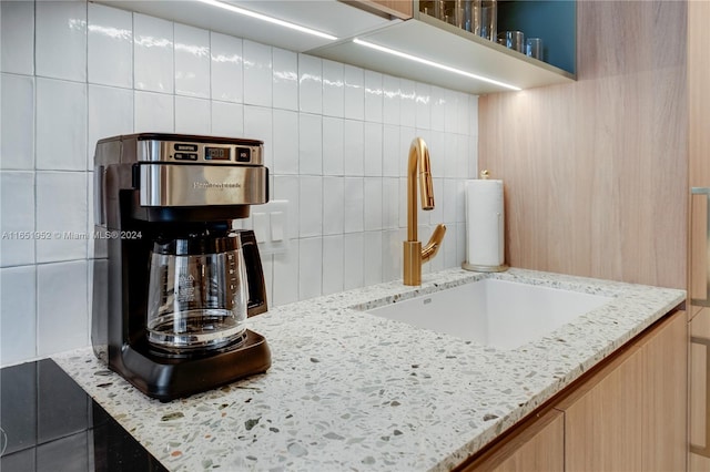 kitchen featuring light brown cabinetry, light stone counters, backsplash, and sink