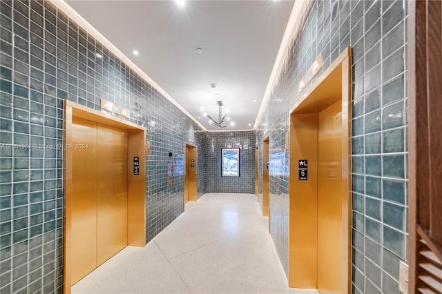 corridor with crown molding, tile walls, a notable chandelier, and elevator