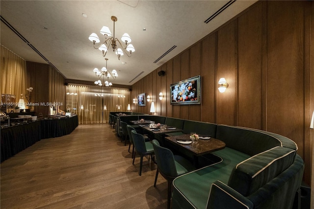 dining area featuring a chandelier, wood-type flooring, and wooden walls