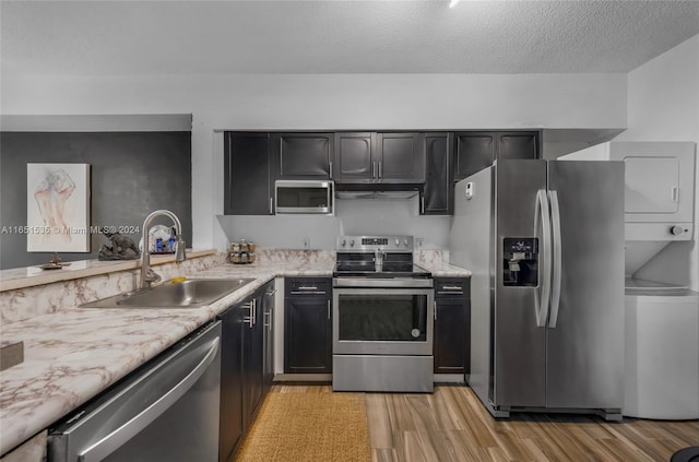 kitchen with light wood-type flooring, stacked washer and dryer, a textured ceiling, sink, and appliances with stainless steel finishes