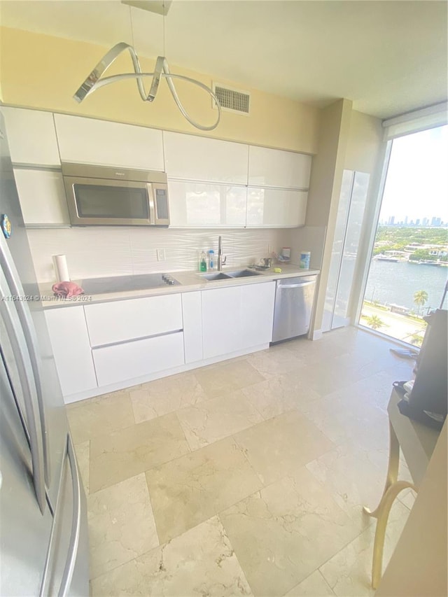 kitchen with white cabinets, pendant lighting, sink, backsplash, and appliances with stainless steel finishes